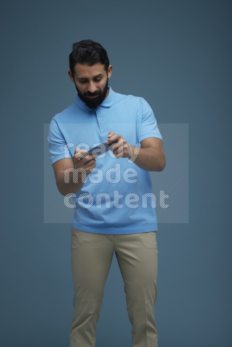 Man playing a game on his phone in a blue background wearing a Blue shirt