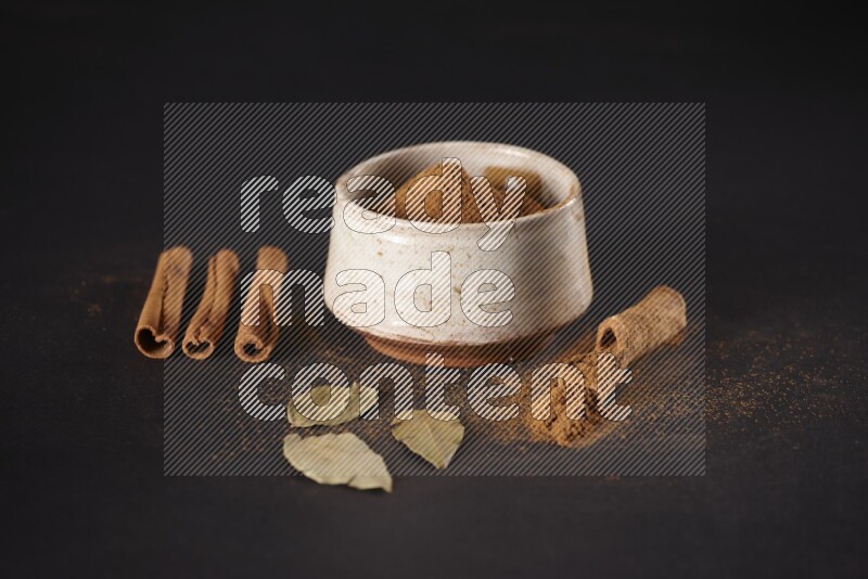 Cinnamon powder in a white pottery bowl and cinnamon sticks and laurel leaves on black background