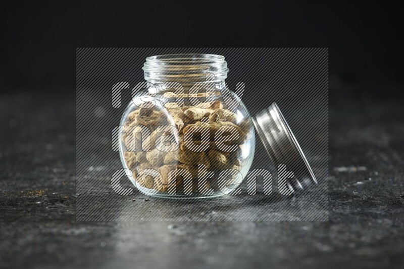 A glass spice jar full of dried turmeric whole fingers on a textured black flooring