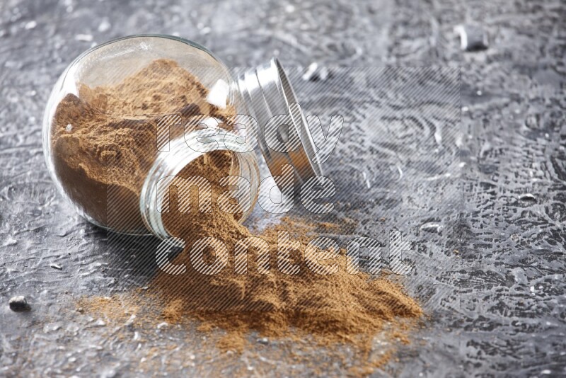 Flipped herbal glass jar full of cinnamon powder on textured black background