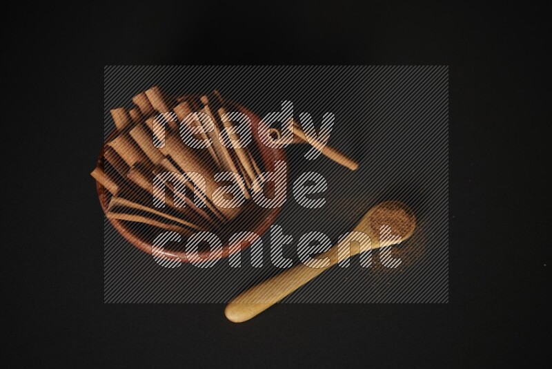 Cinnamon sticks in wooden bowl and cinnamon powder in a wooden spoon on black background