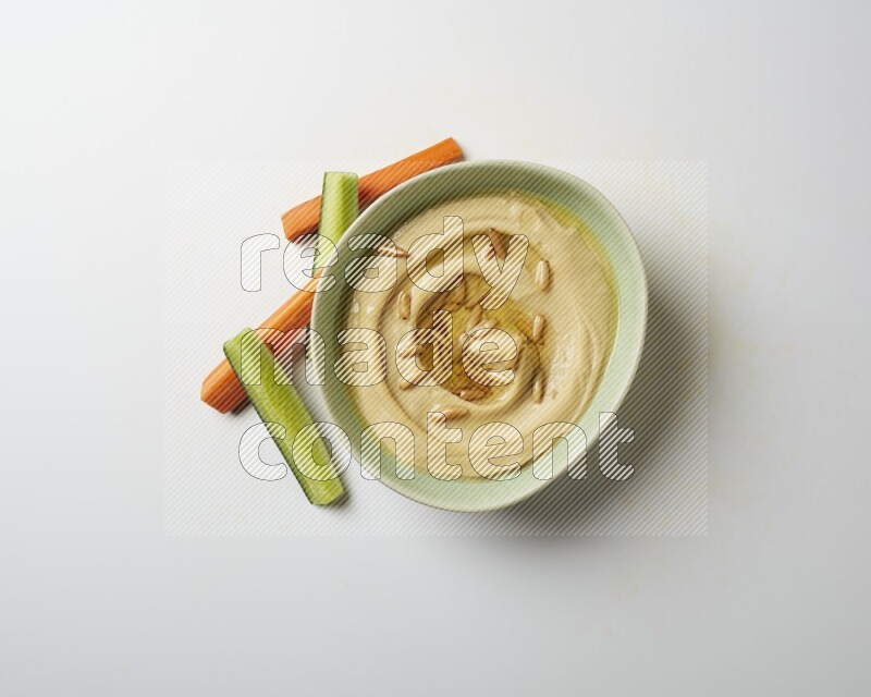 Hummus in a green plate garnished with pine nuts on a white background