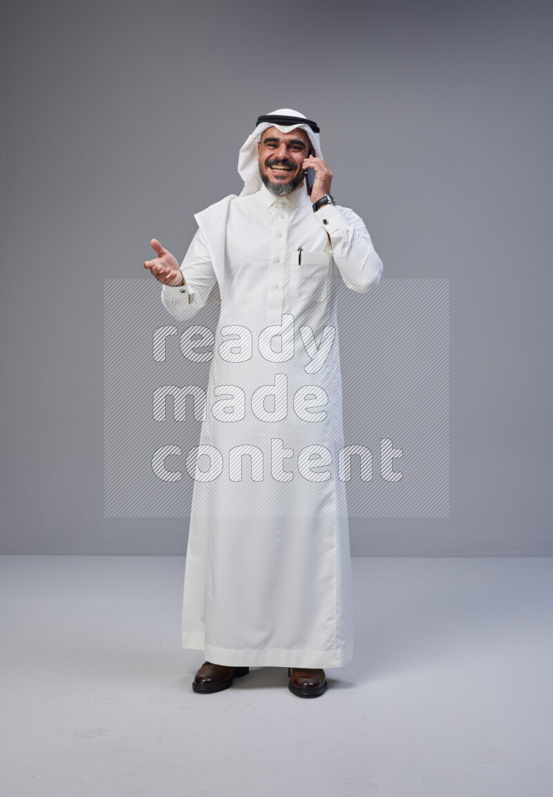 Saudi man Wearing Thob and white Shomag standing talking on phone on Gray background