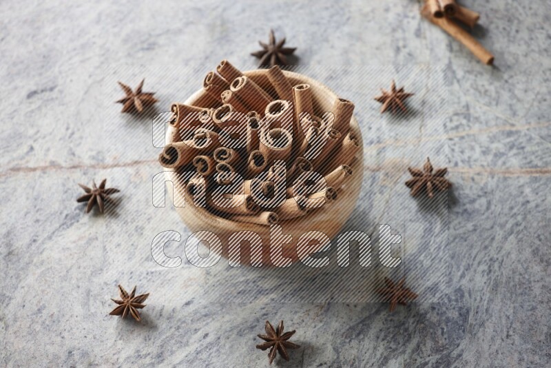 wooden bowl full of cinnamon sticks surrounded by star anis on marble background in different angles