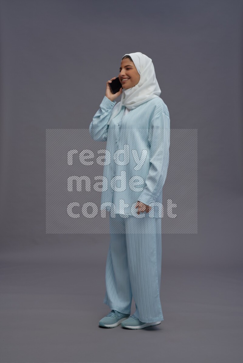 Saudi woman wearing hijab clothes standing talking on phone on gray background