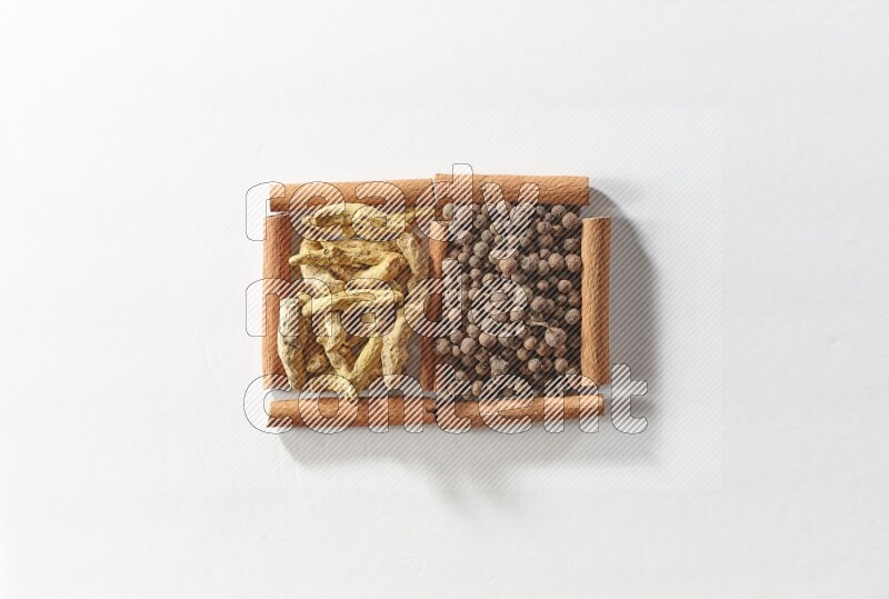 مربعان من أعواد القرفة ممتلئان ببهار الفلفل الحلو وأصابع الكركم علي خلفية بيضاء