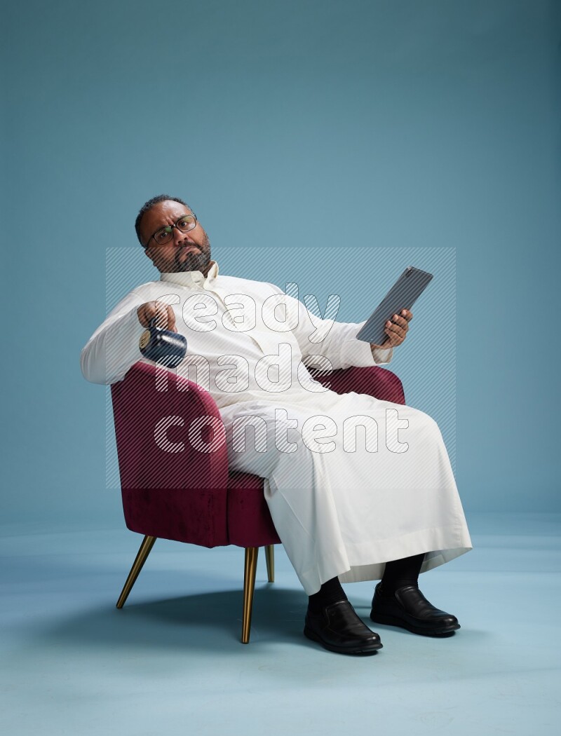 Saudi Man without shimag sitting on chair working on tablet on blue background
