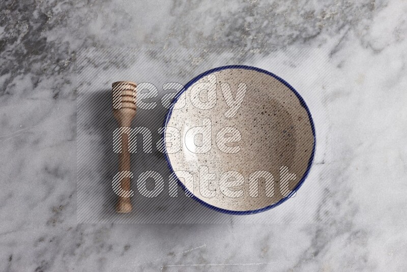 Multicolored pottery bowl with wooden honey dipper on the side on grey marble background