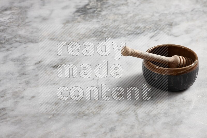 Multicolored pottery bowl with wooden honey dipper in it on grey marble background