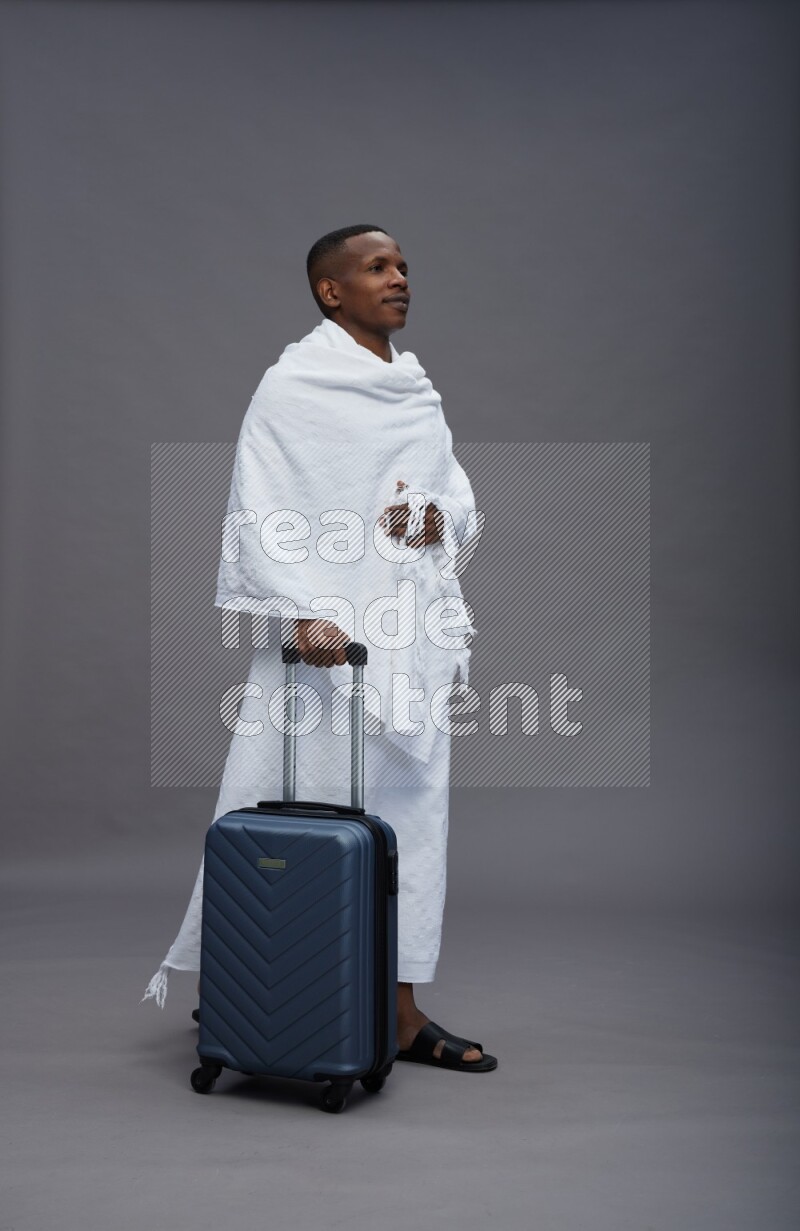A man wearing Ehram Standing holding traveling bag on gray background
