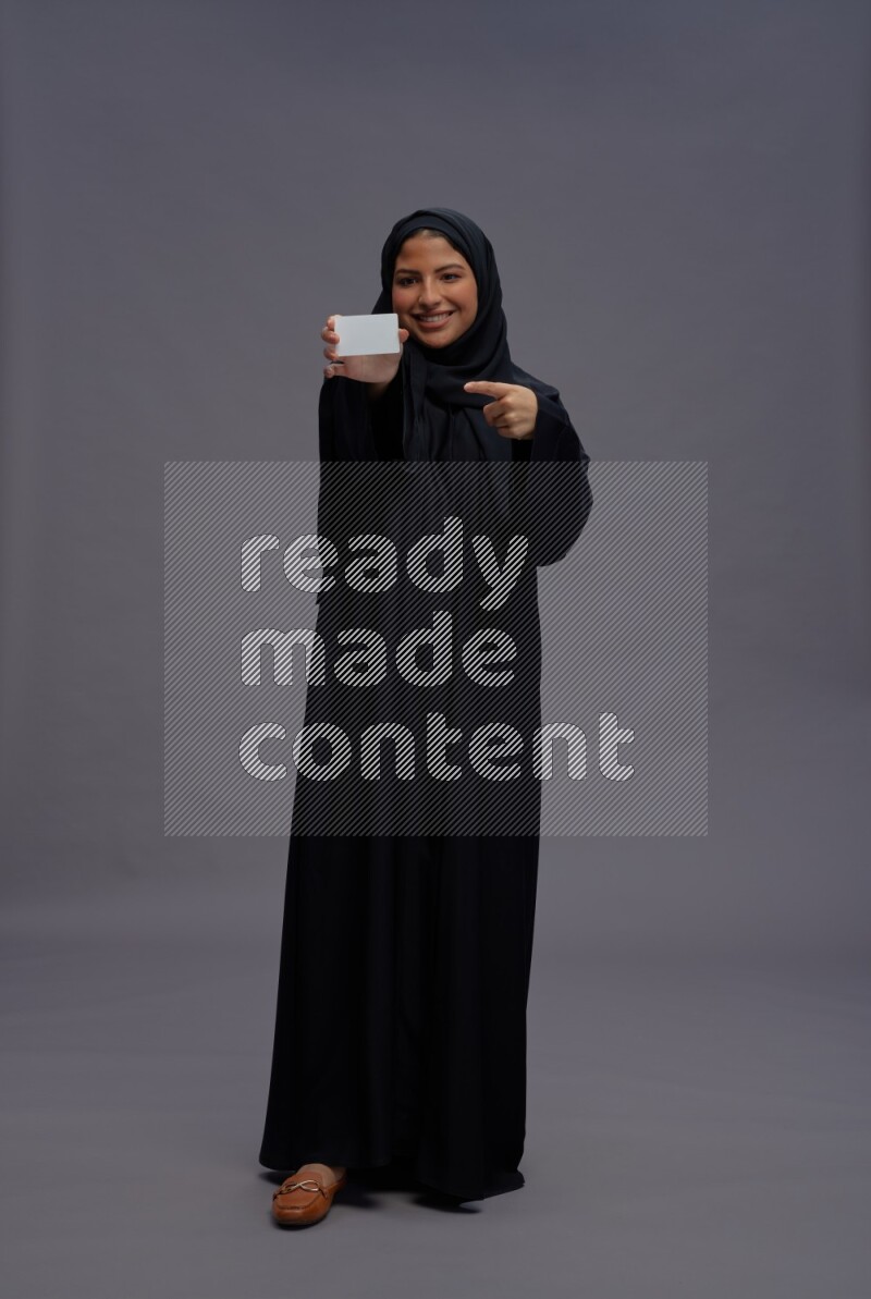 Saudi woman wearing Abaya standing holding ATM card on gray background