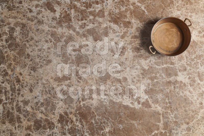 A small copper pan on beige marble background