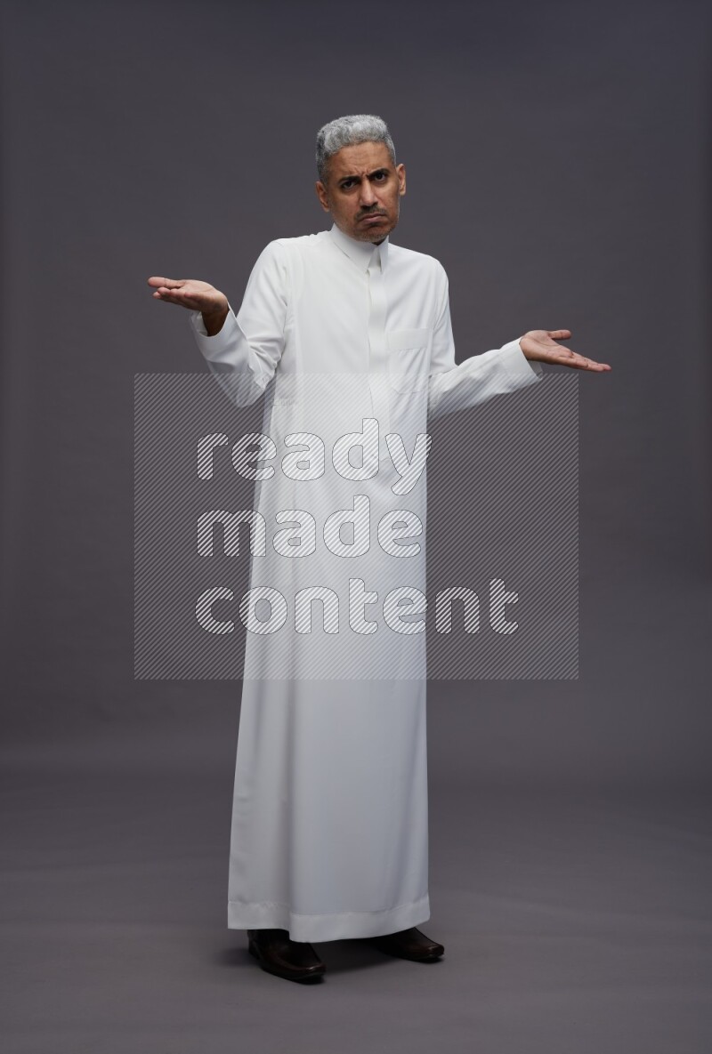 Saudi man wearing thob standing interacting with the camera on gray background