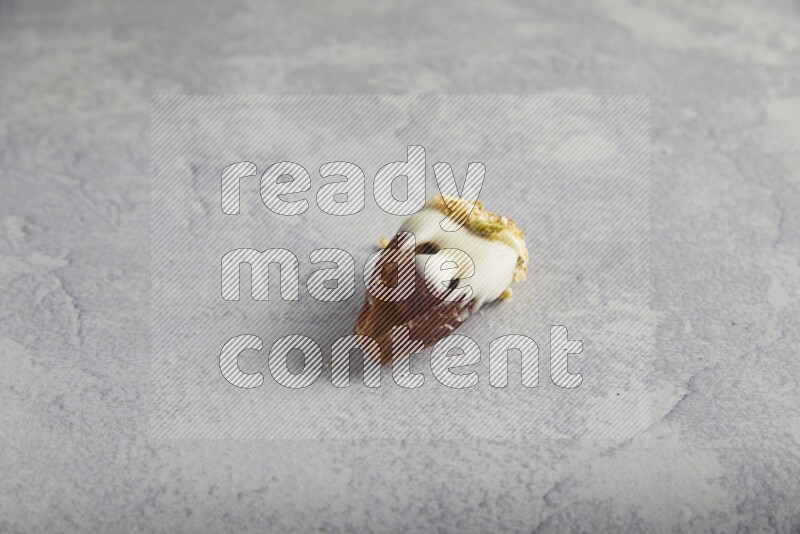 Hazulnut stuffed date covered with white chocolate and crushed peanuts & pistachios on light grey background