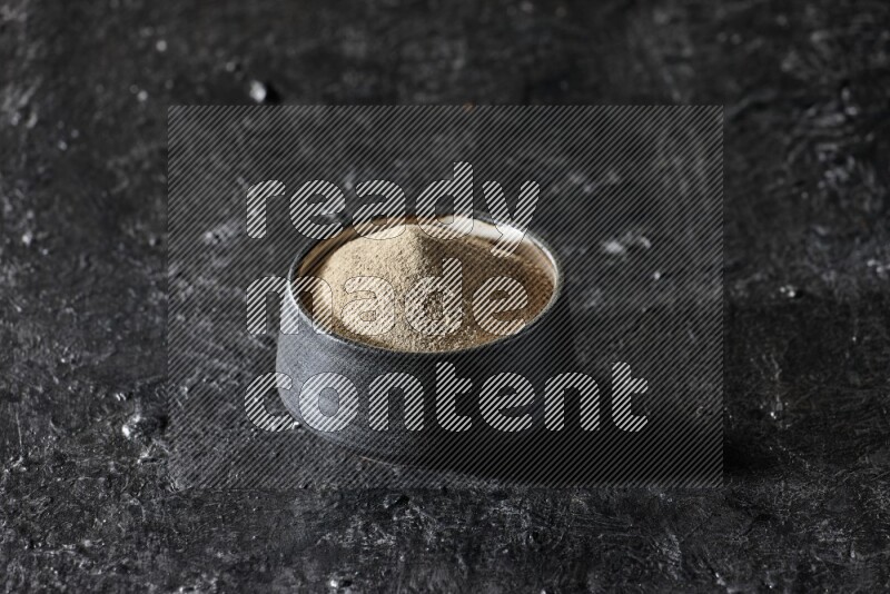 Black pottery bowl full of white pepper powder on textured black flooring