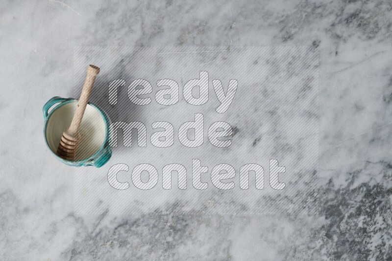 Multicolored pottery bowl with wooden honey dipper in it on grey marble background
