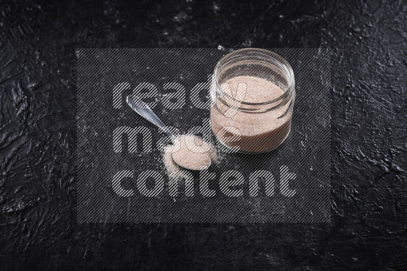 A glass jar full of fine himalayan salt on black background