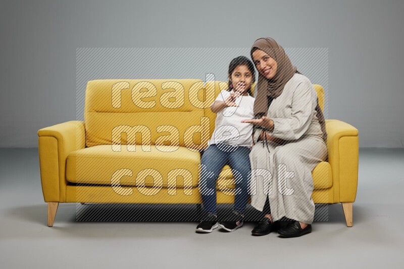Mom and daughter sitting on sofa holding ATM card on gray background