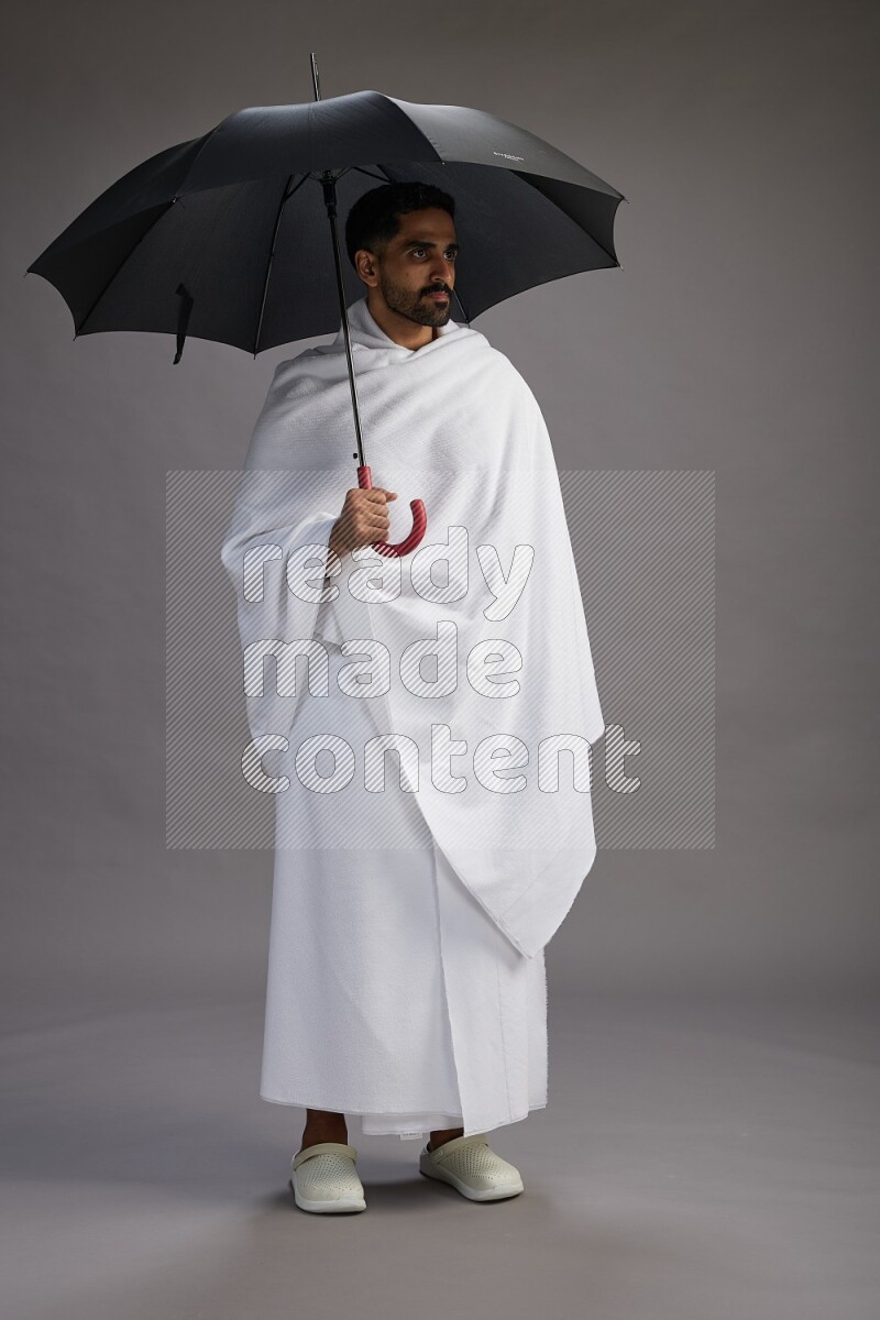 A man wearing Ehram Standing holding umbrella on gray background