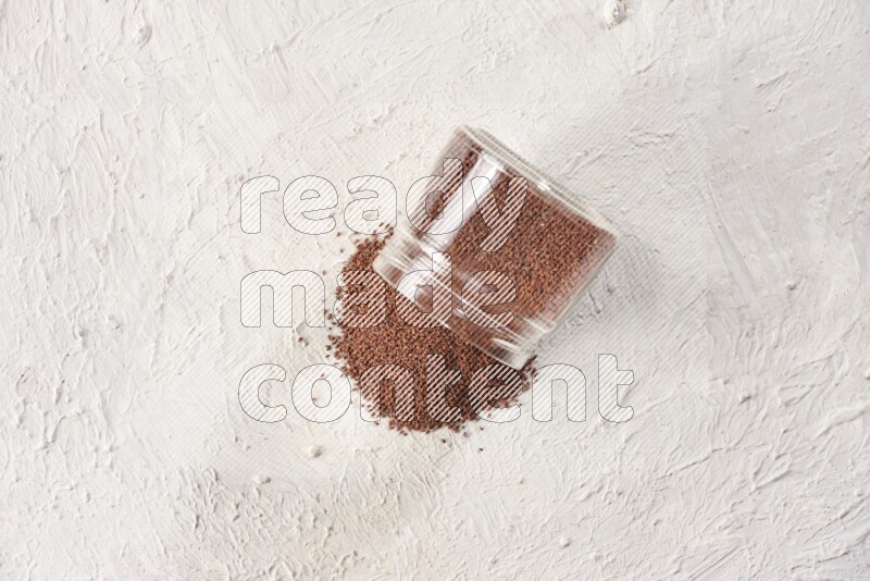 A glass jar full of garden cress seeds and jar is flipped and seeds are spread on a textured white flooring
