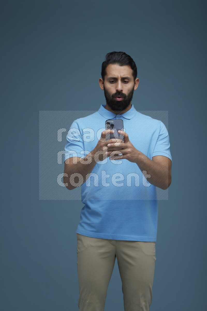 A man Texting on his phone in a blue background wearing a Blue shirt
