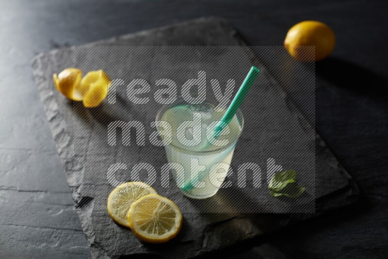 A glass of lemon juice with a straw on black background