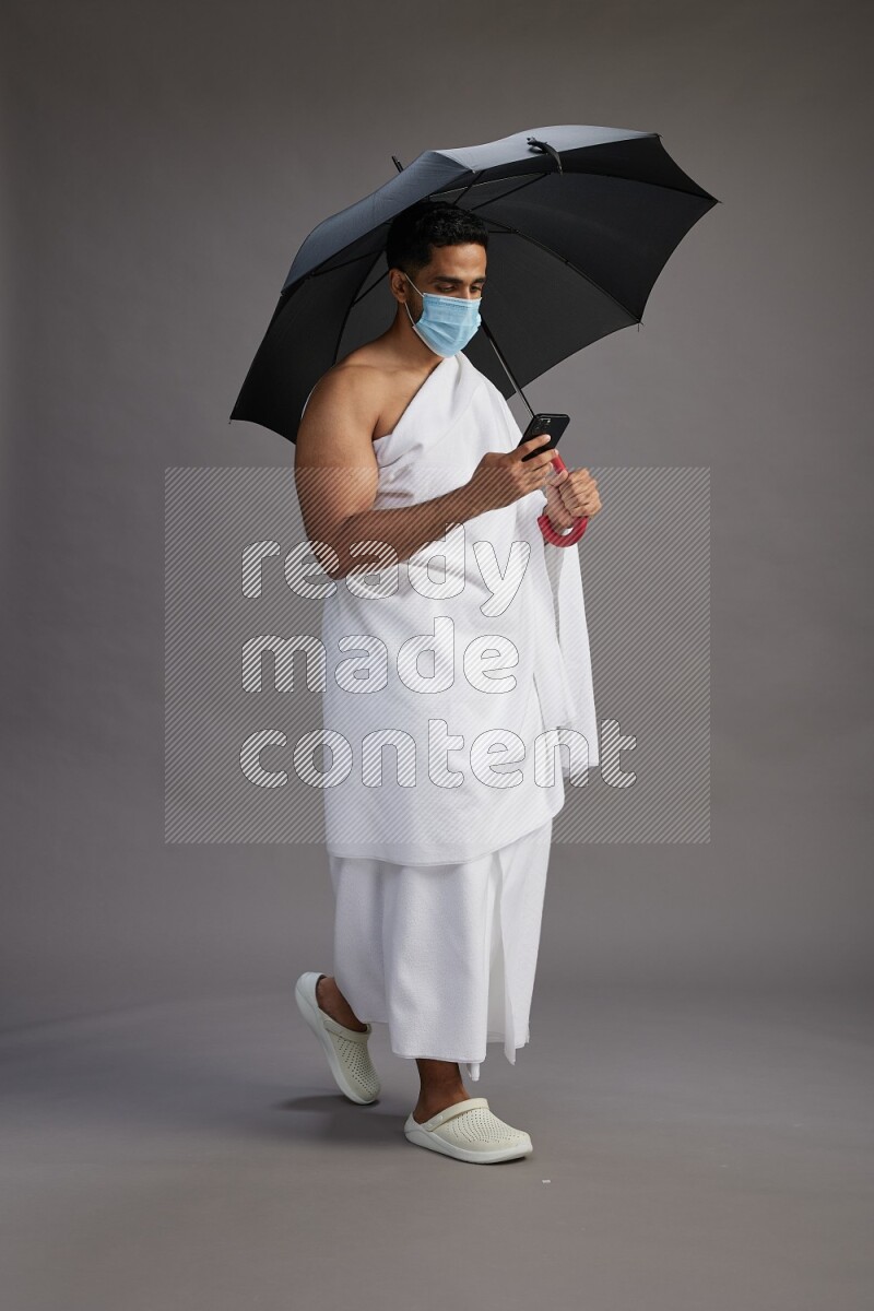 A man wearing Ehram and mask Standing holding umbrella on gray background on gray background