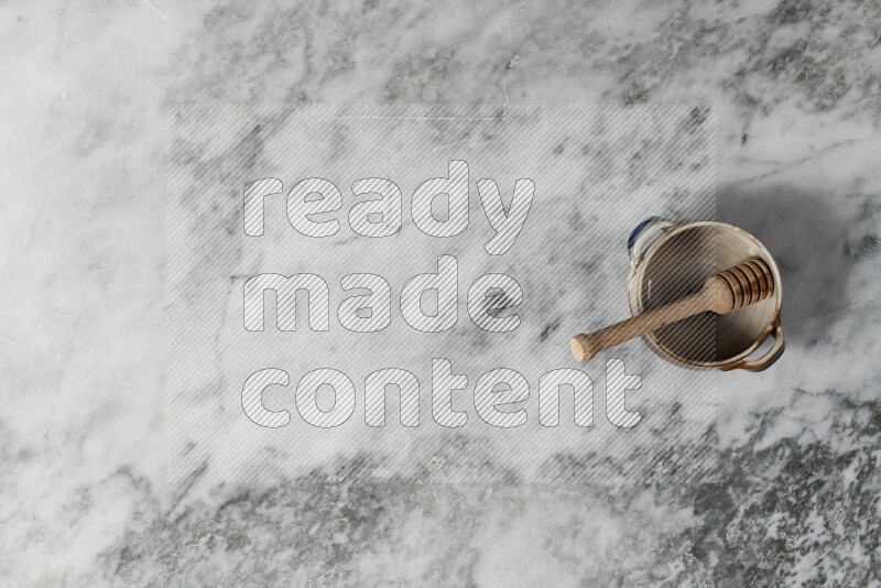 Multicolored pottery bowl with wooden honey dipper in it on grey marble background