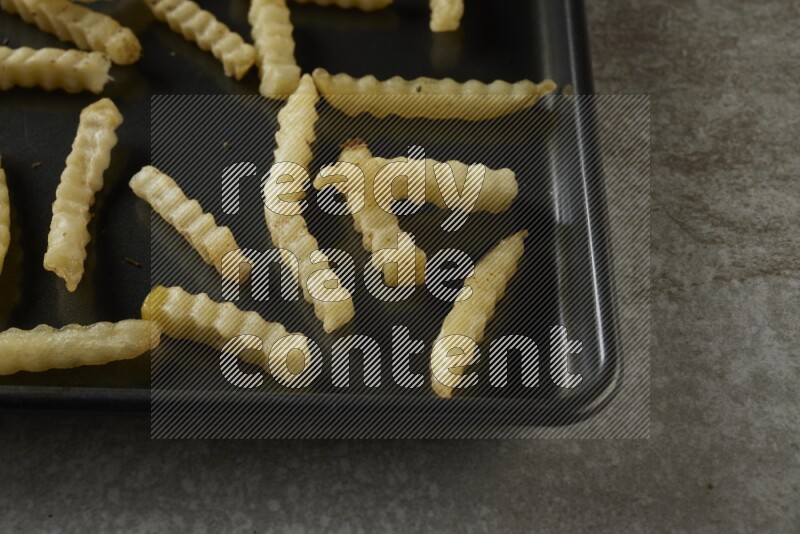 crinkle fries in a black stainless steel rectangle tray on grey textured counter top