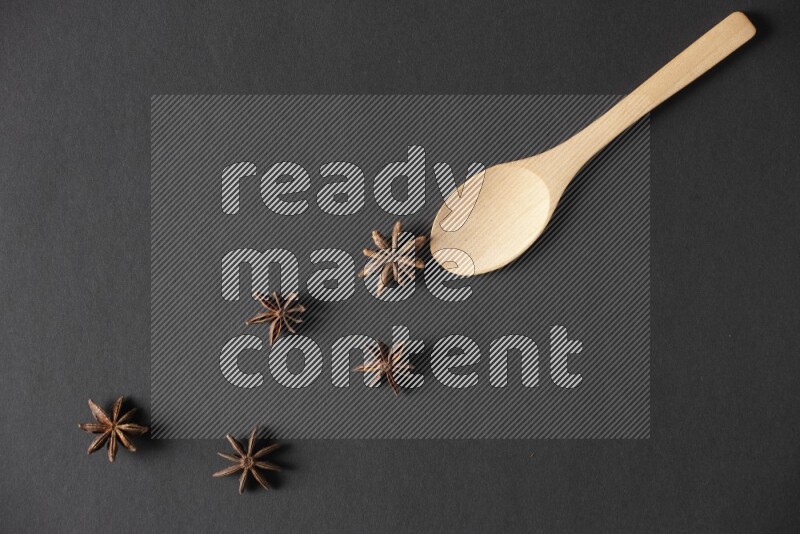 Star Anise in a wooden spoon on more stars anise filling the frame on black flooring