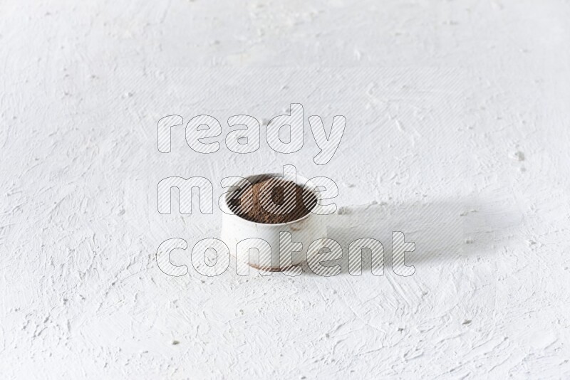 A beige ceramic bowl full of cloves powder on a white flooring