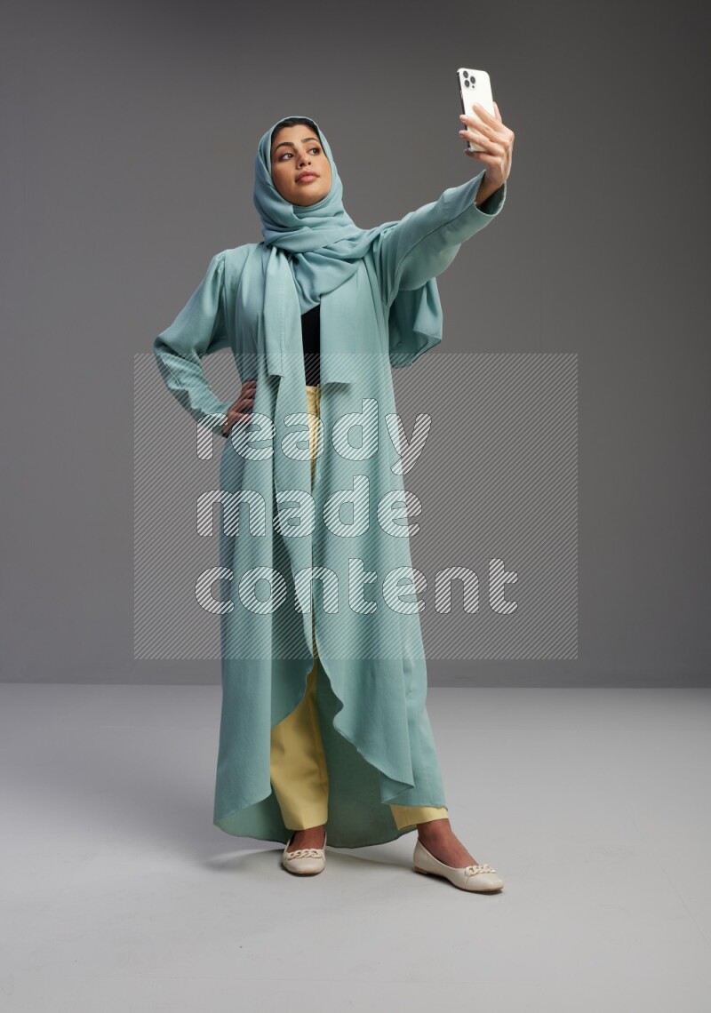 Saudi Woman wearing Abaya standing taking selfie on Gray background