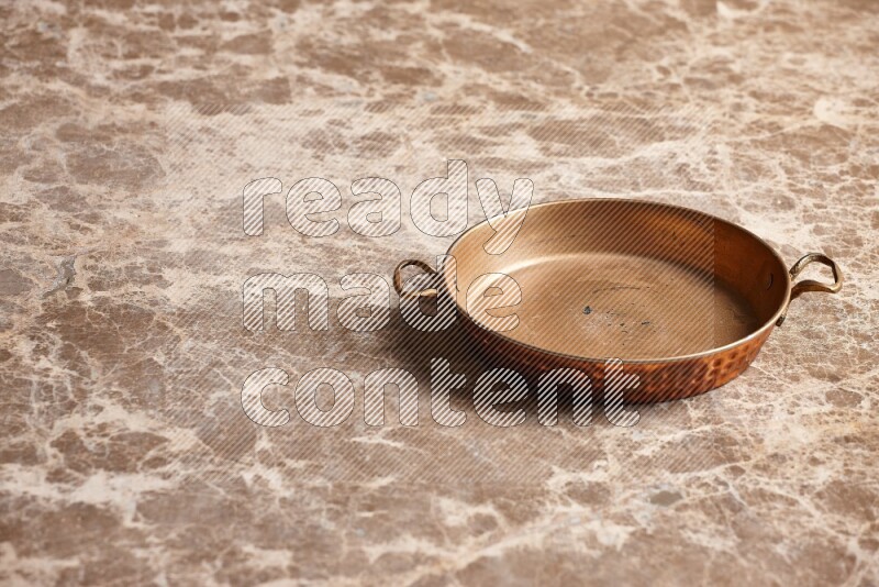 A small copper pan on beige marble background