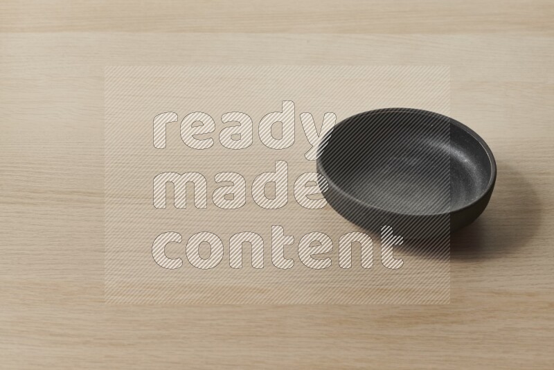 A black pottery bowl on light wooden background