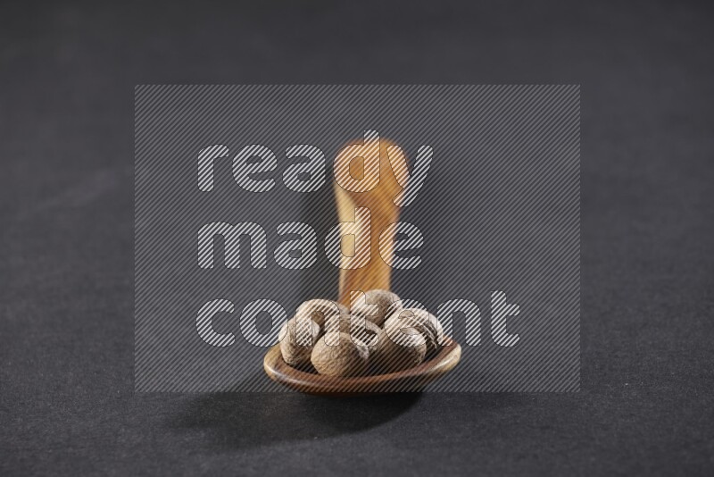 A wooden ladle full of whole nutmeg seeds on a black flooring