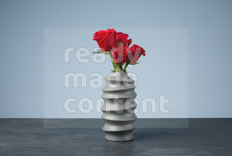 An arrangement of vivid red roses in a grey spiral vase on black marble background