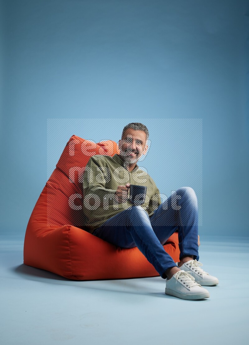 A man sitting on an orange beanbag and drinking coffee