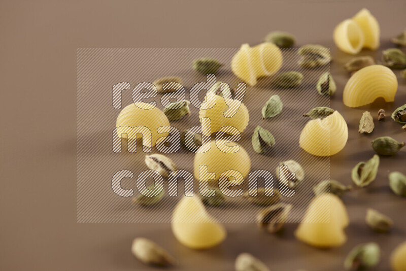 Raw pasta with different ingredients such as cherry tomatoes, garlic, onions, red chilis, black pepper, white pepper, bay laurel leaves, rosemary and cardamom on beige background