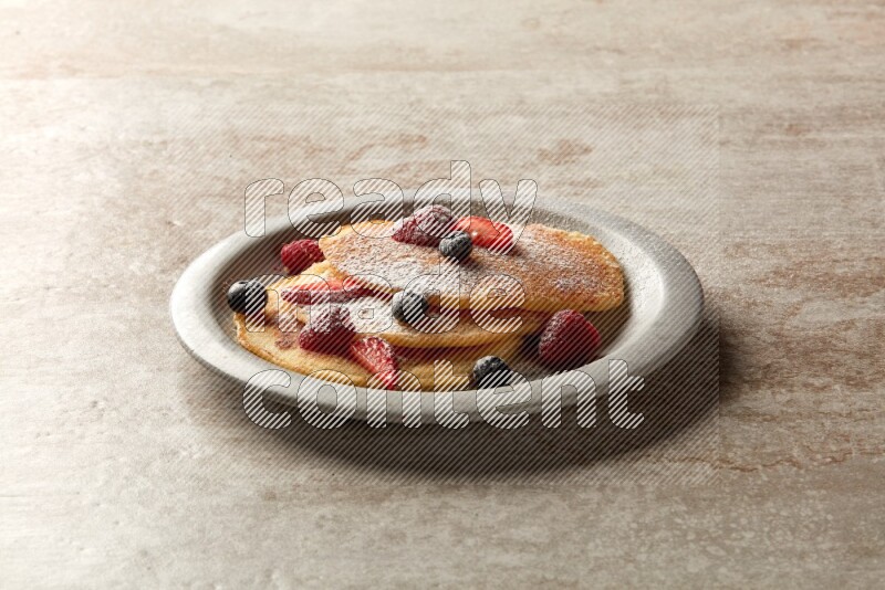 Three stacked mixed berries pancakes in a grey plate on beige background