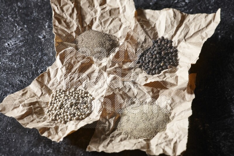 Crumpled pieces of paper full of black and white pepper beads and powder on a textured black flooring