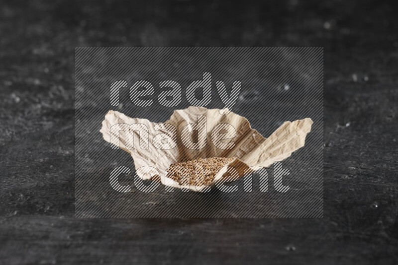 A crumpled piece of paper full of mustard seeds on a textured black flooring