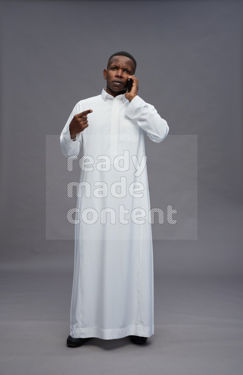 Saudi man wearing thob standing talking on phone on gray background