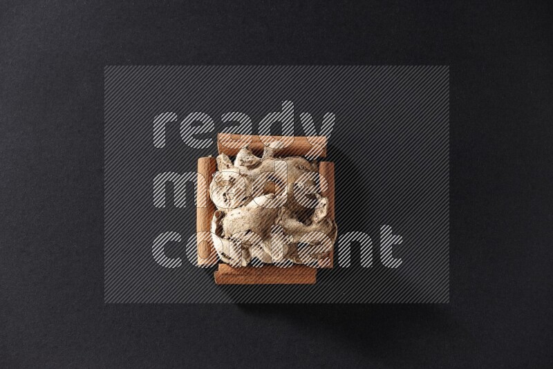 A single square of cinnamon sticks full of dried ginger on black flooring