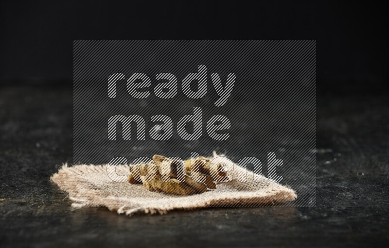 Dried turmeric whole fingers on a burlap piece of fabric on textured black flooring