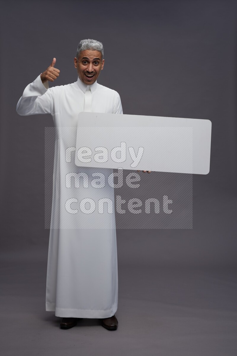 Saudi man wearing thob standing holding board on gray background