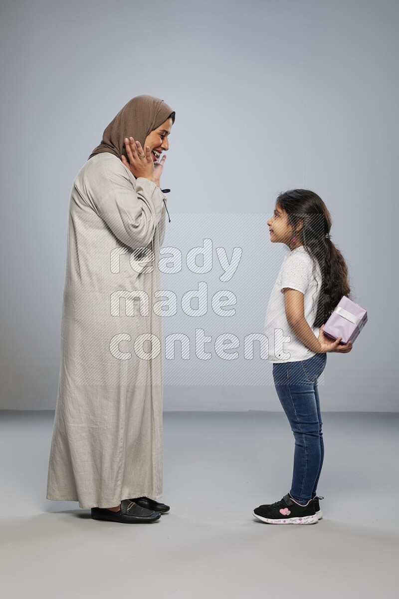 A girl standing hiding a gift behind her back for her mother on gray background