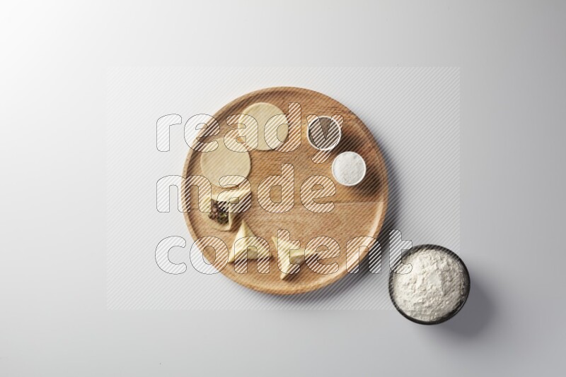 two closed sambosas and one open sambosa filled with meat while flour, salt, and black pepper aside in a wooden dish on a white background