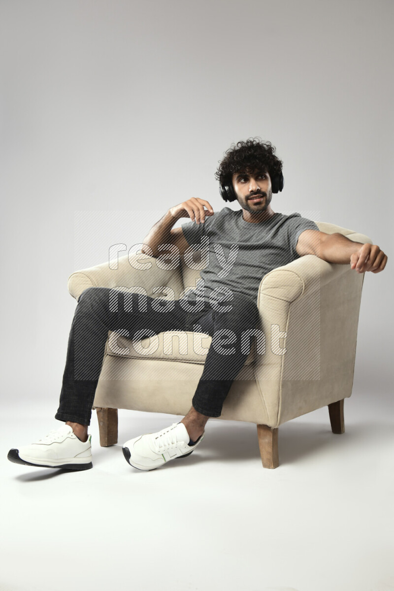 A man wearing casual sitting on a chair putting on headphones on white background