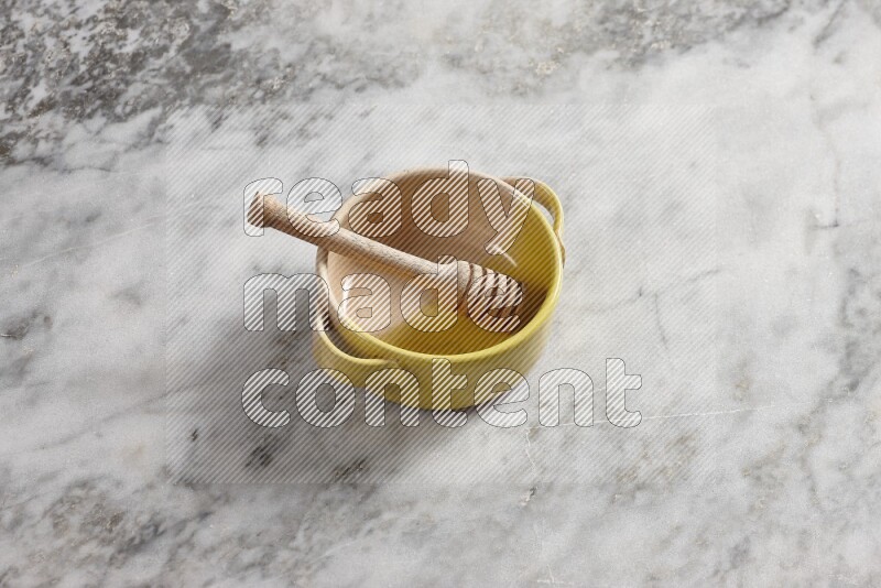 Multicolored pottery bowl with wooden honey dipper in it on grey marble background