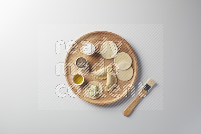 two closed sambosas and one open sambosa filled with cheese while salt, black pepper and oil with oil brush aside in a wooden dish on a white background